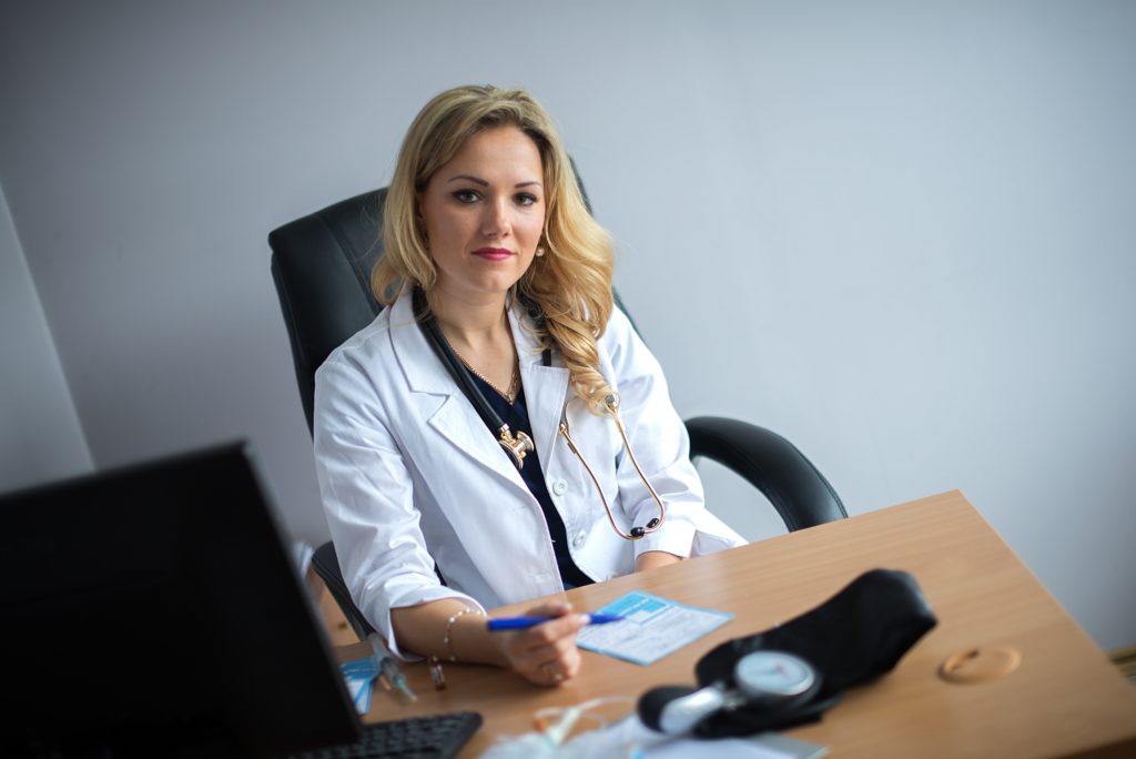 Retrato de uma jovem médica sorridente sentada à mesa em um hospital ou clínica particular